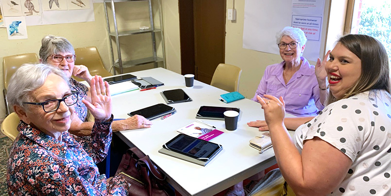 Digital health mentor Kirstie teaches a class of women with tablets on the table.