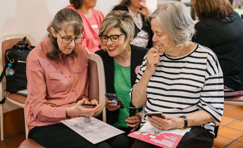 Two Get Online Week event participants chatting and looking a phone with Good Things CEO, Jess Wilson