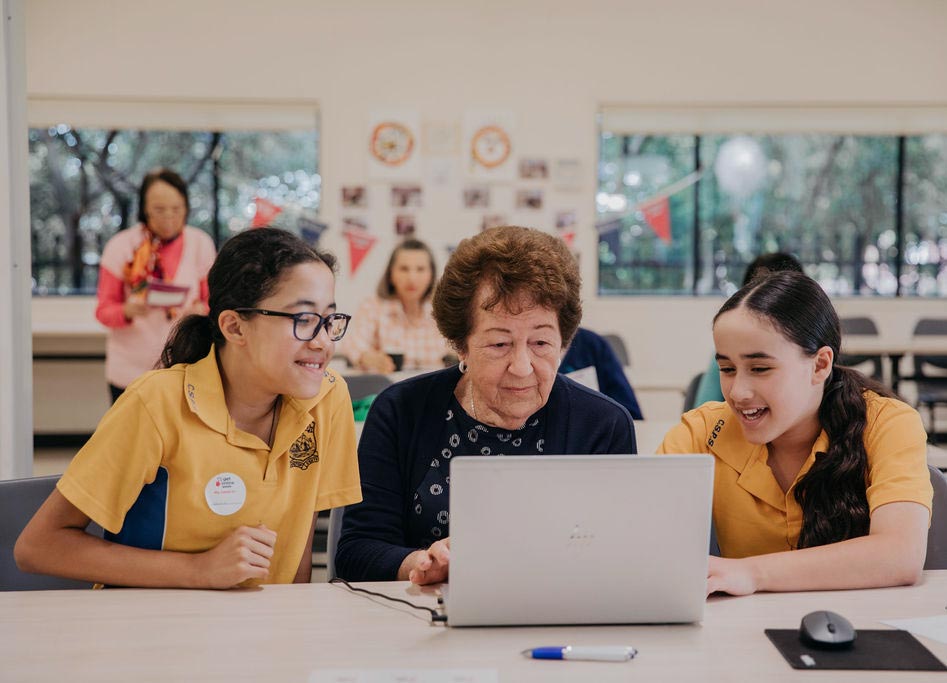 2 school students help an older woman on her laptop