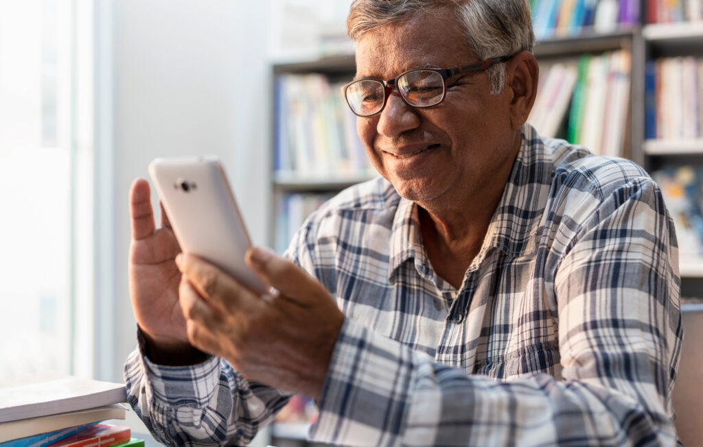 Happy elderly Asian man using smartphone at home.