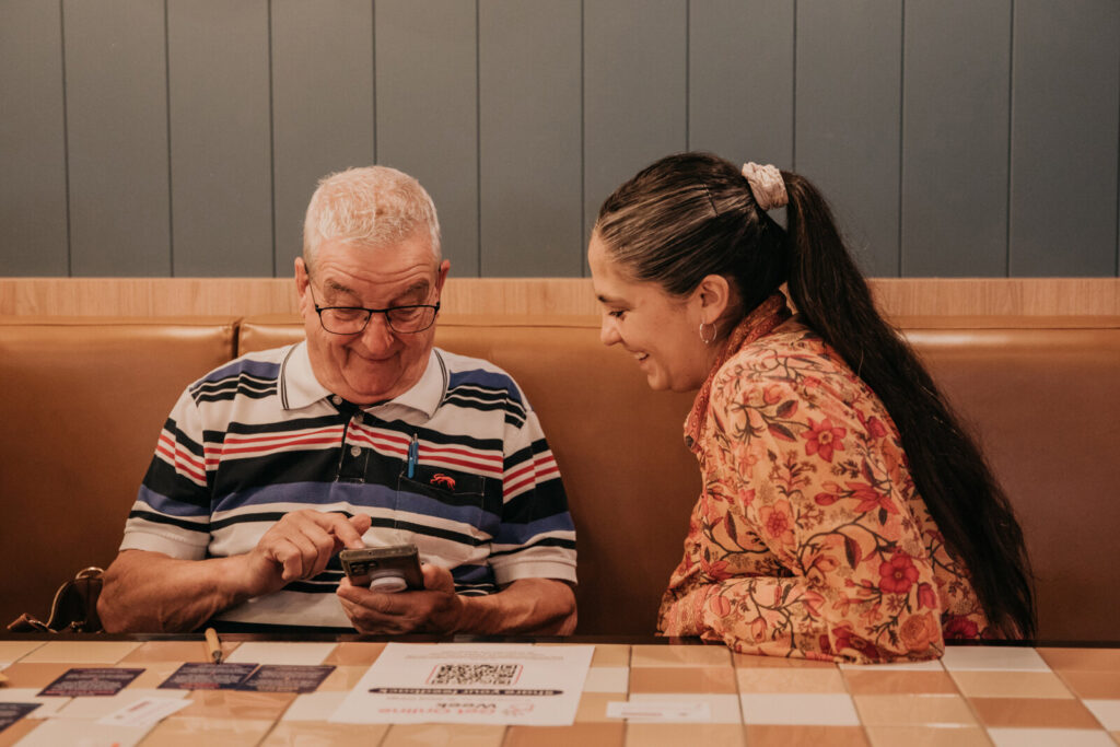 An elder learning how to use his phone and laughing with a women supporting him.