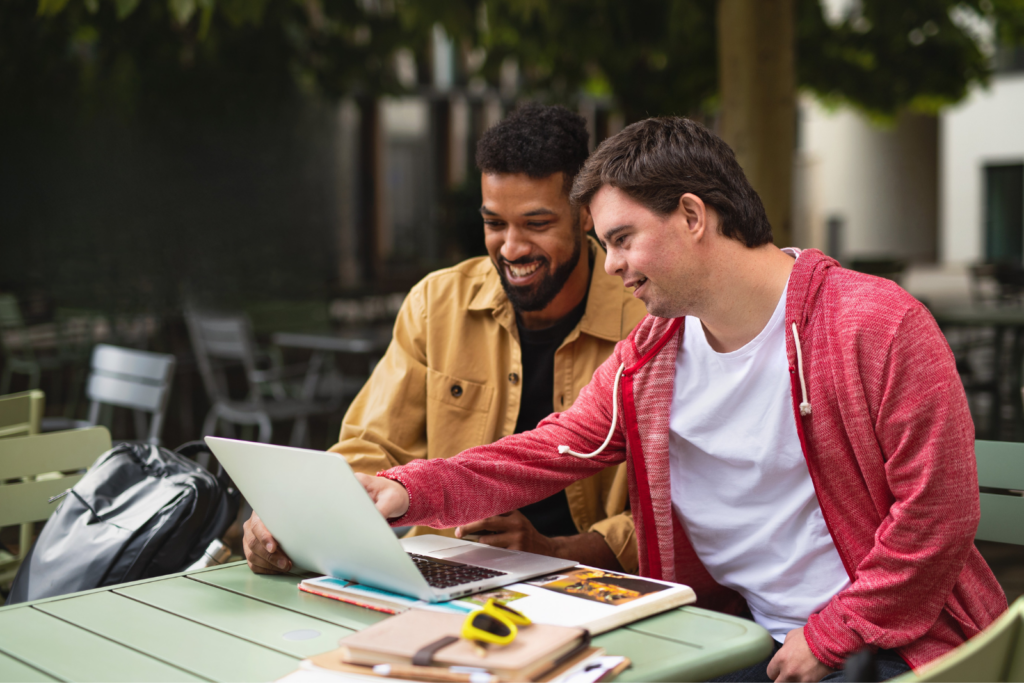 A men with intellectual disability and another men smiling and using a laptop